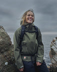 woman in laurel green windbreaker jacket with hood resting on a stone